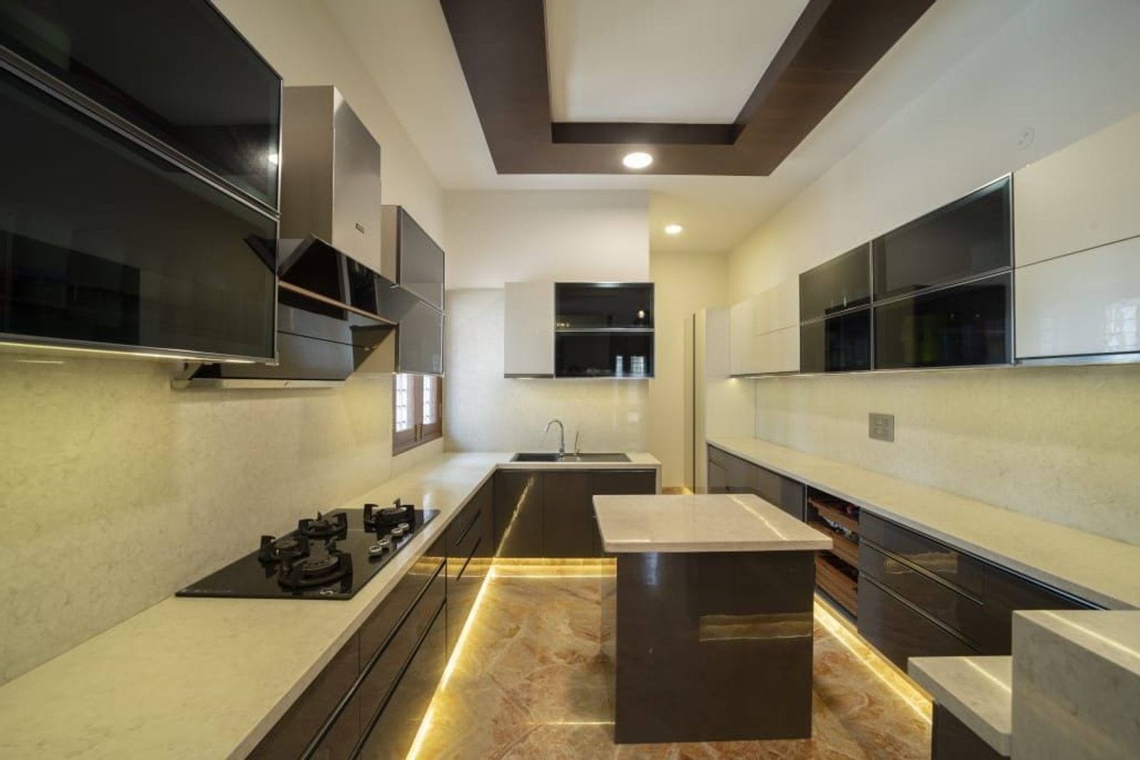 A galley kitchen in dark and white cabinets, an island lit along its base