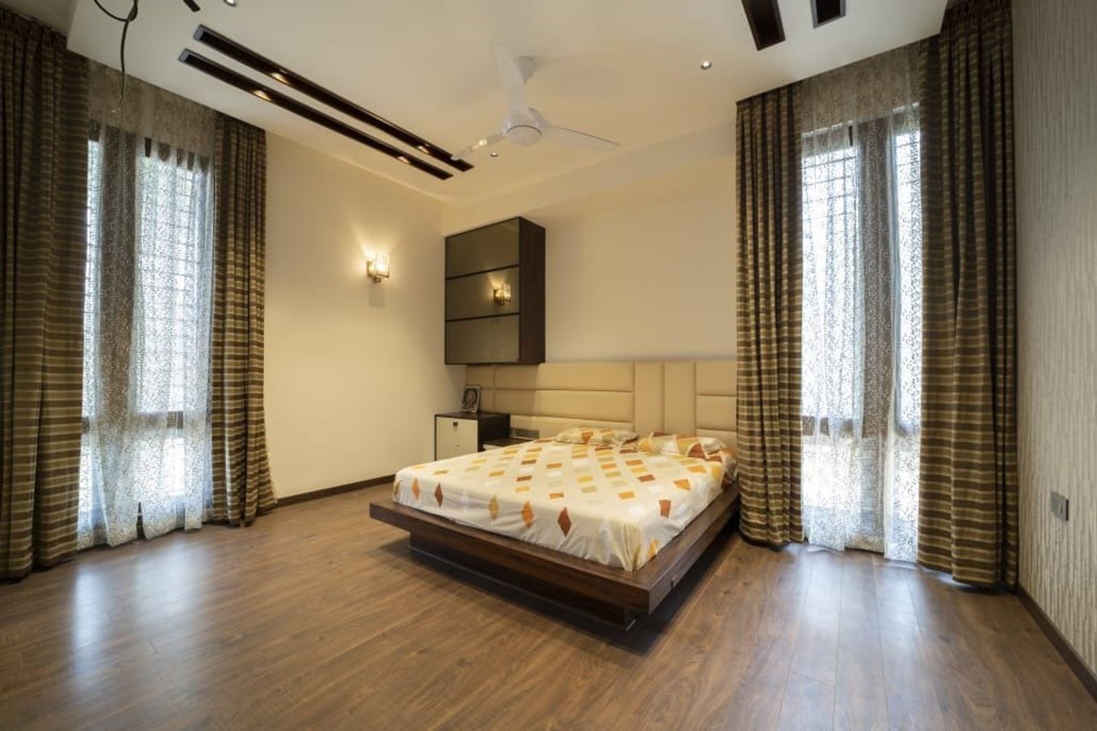A bedroom with a timber bed and a panelled headboard wall, tall curtains either side