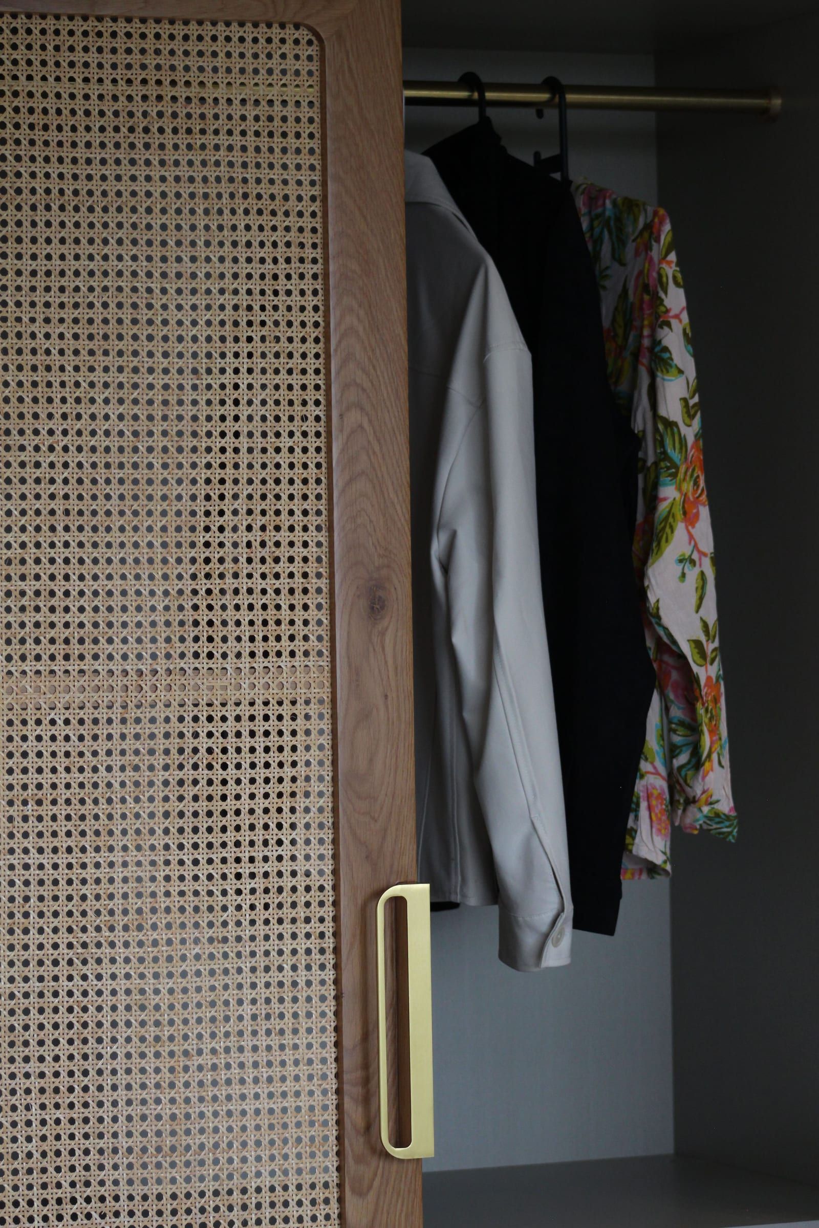 A timber wardrobe door with a cane panel and a brushed brass edge pull