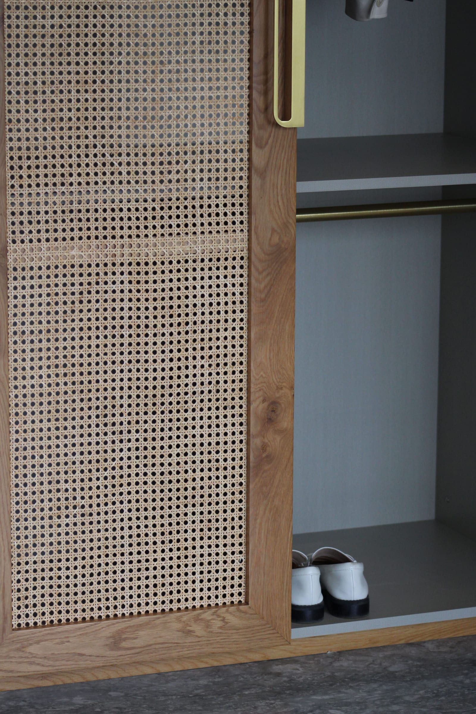 A timber wardrobe door with a cane panel and a brass pull, clothes hanging beside it