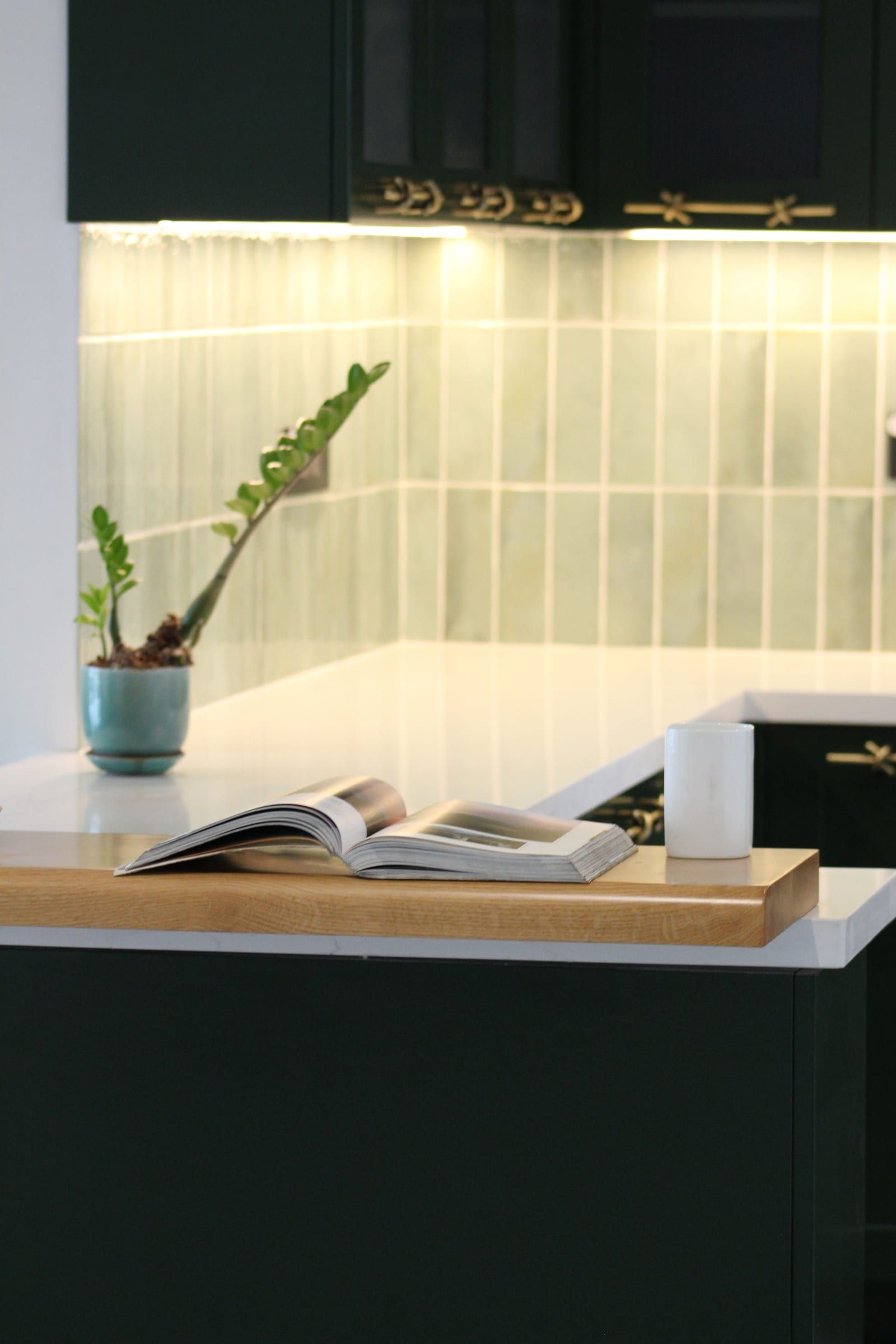 A dark green kitchen counter with sage tiles and a timber ledge on a white worktop