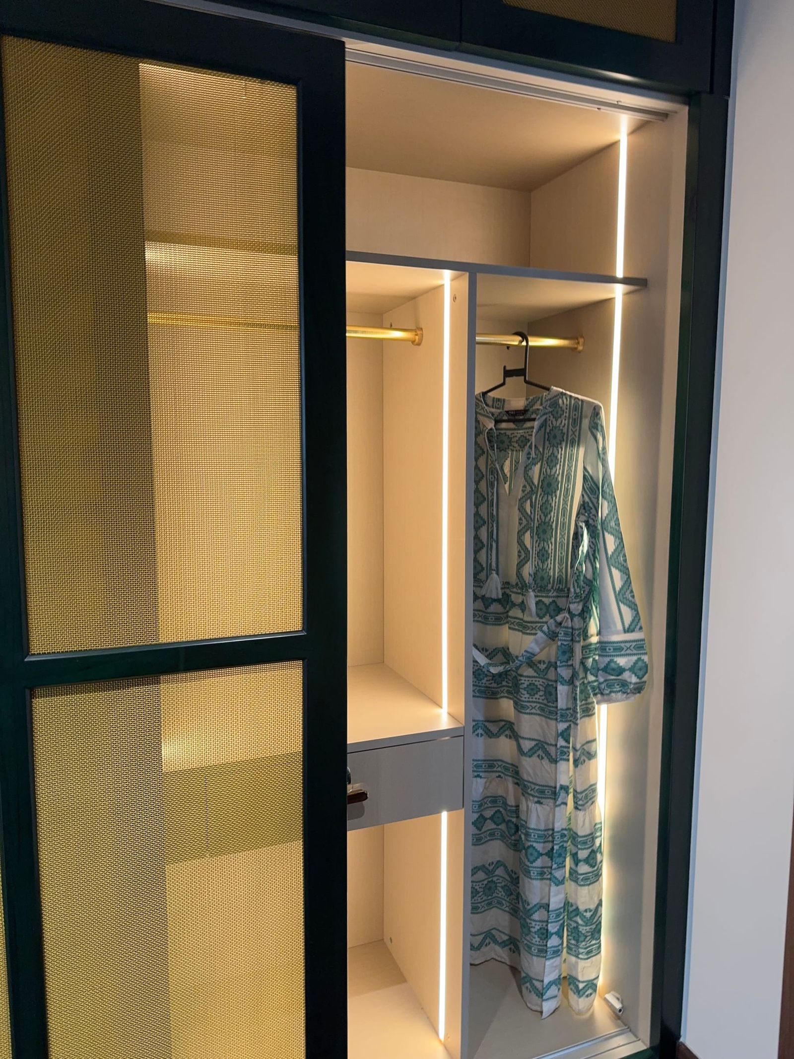 A wardrobe door in a dark green frame, cane set into it, the compartment behind lit from within